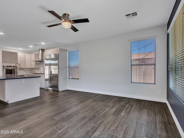 unfurnished living room with dark wood-style floors, baseboards, visible vents, and a ceiling fan