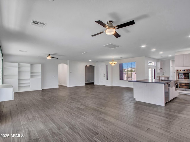 unfurnished living room featuring visible vents, arched walkways, dark wood-type flooring, a sink, and ceiling fan with notable chandelier