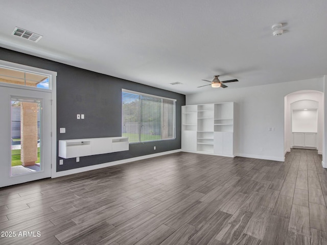 unfurnished living room with arched walkways, wood finished floors, visible vents, and a ceiling fan