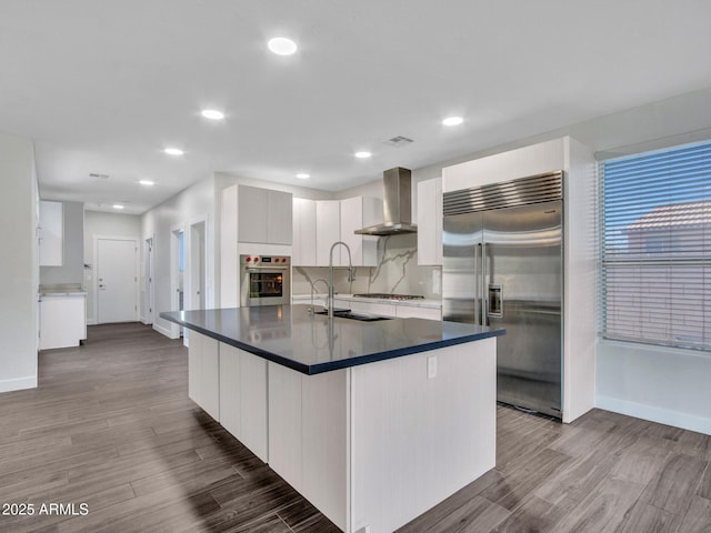 kitchen with dark countertops, backsplash, appliances with stainless steel finishes, wall chimney range hood, and wood finished floors