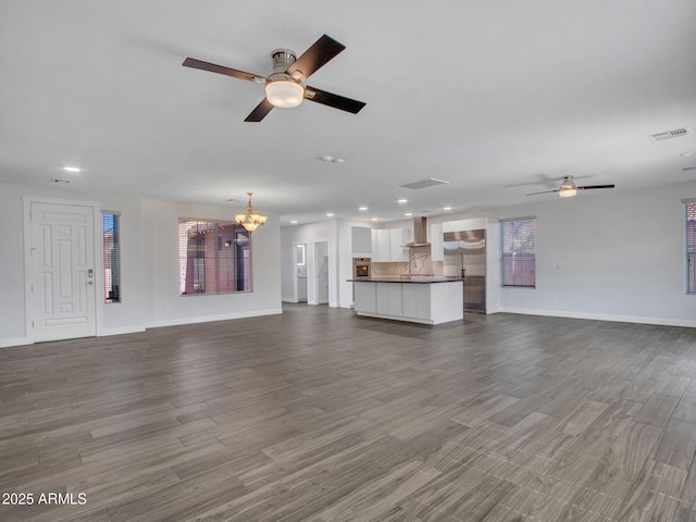 unfurnished living room featuring baseboards, visible vents, dark wood-type flooring, and ceiling fan with notable chandelier