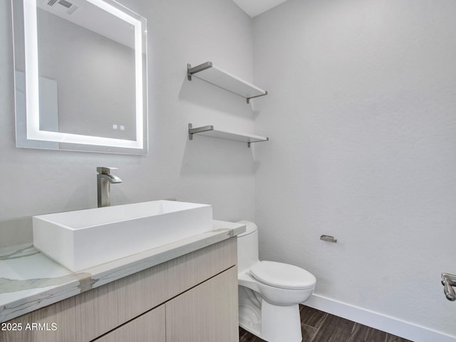 bathroom with visible vents, toilet, vanity, wood finished floors, and baseboards