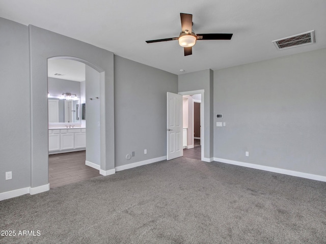 unfurnished bedroom featuring arched walkways, dark carpet, visible vents, and baseboards