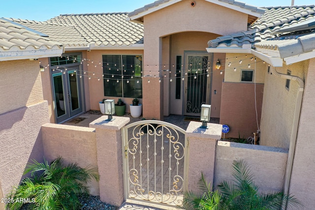 entrance to property with a tiled roof, french doors, fence, and stucco siding