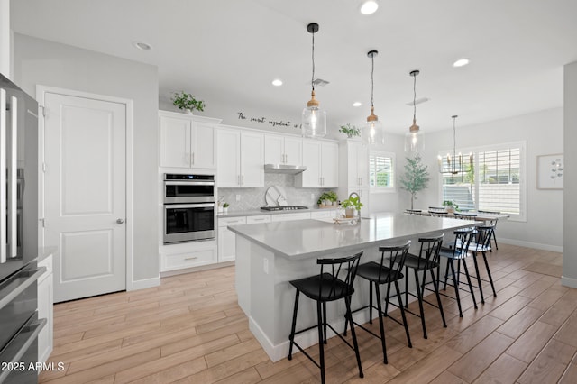 kitchen with baseboards, a breakfast bar area, under cabinet range hood, light wood finished floors, and appliances with stainless steel finishes