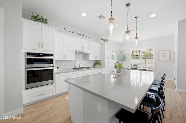 kitchen with a breakfast bar area, backsplash, visible vents, light countertops, and baseboards