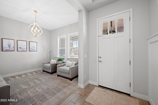 foyer featuring baseboards, light wood-type flooring, and a chandelier