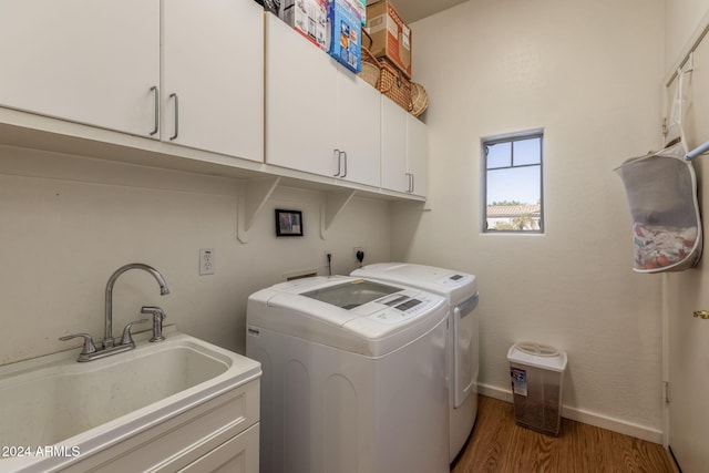 clothes washing area featuring washing machine and dryer, sink, cabinets, and hardwood / wood-style flooring