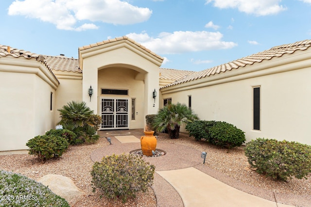 doorway to property with a patio area, a tile roof, and stucco siding