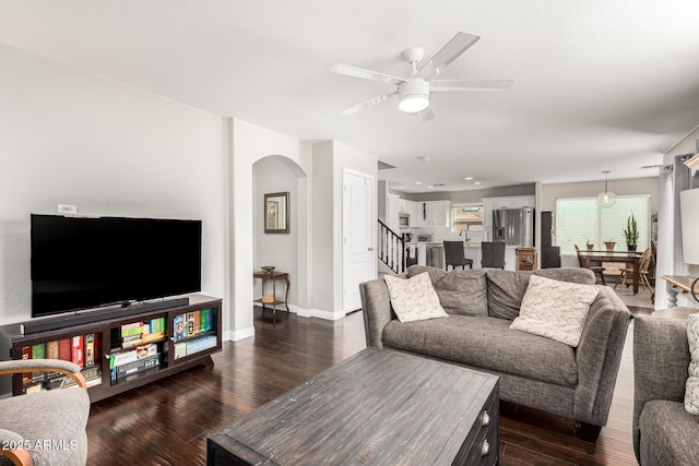 living room featuring dark wood-type flooring, baseboards, arched walkways, and ceiling fan