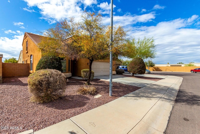 view of front of house featuring stucco siding, a garage, concrete driveway, and fence