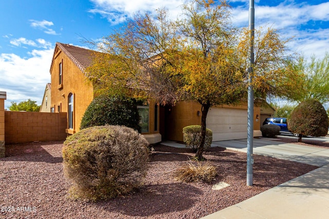 view of front facade featuring stucco siding, an attached garage, driveway, and fence