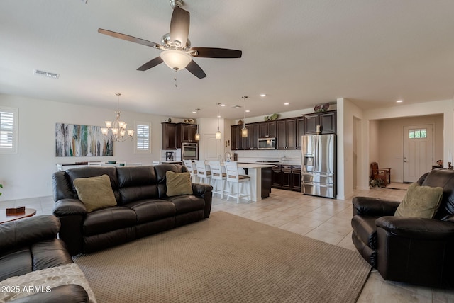 living area featuring light tile patterned flooring, visible vents, recessed lighting, and ceiling fan with notable chandelier