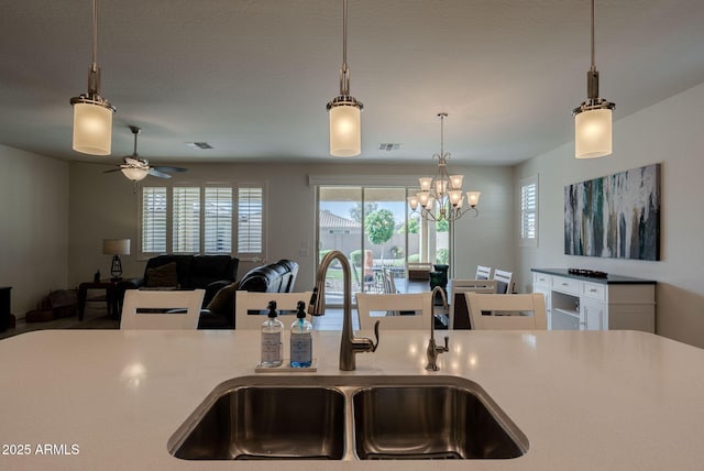kitchen featuring hanging light fixtures, light countertops, a sink, and ceiling fan with notable chandelier
