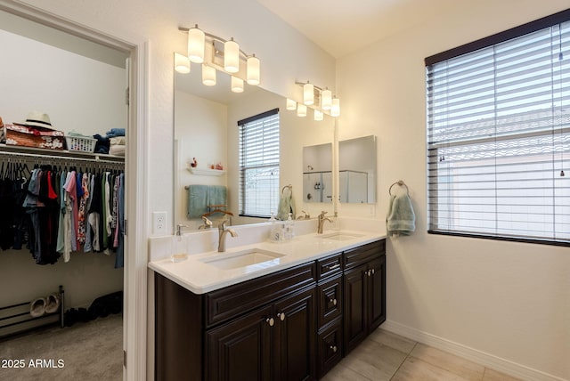 bathroom with double vanity, a walk in closet, a sink, and tile patterned floors
