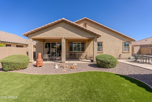 rear view of property featuring a lawn, stucco siding, fence, and a patio