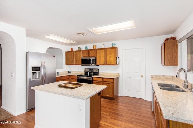 kitchen featuring light hardwood / wood-style flooring, stainless steel appliances, light stone counters, a center island, and sink