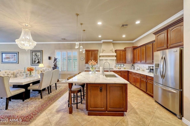 kitchen featuring a center island with sink, stainless steel refrigerator with ice dispenser, visible vents, custom range hood, and backsplash