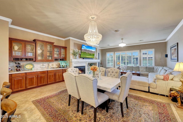 dining space with a chandelier, a glass covered fireplace, visible vents, and crown molding