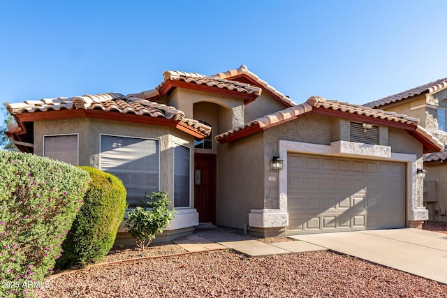 mediterranean / spanish-style home featuring a garage, concrete driveway, stucco siding, and a tiled roof