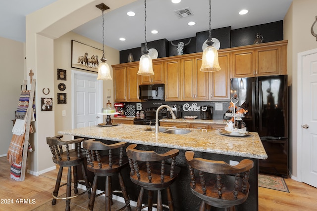 kitchen with decorative backsplash, black appliances, light wood-type flooring, and a kitchen island with sink