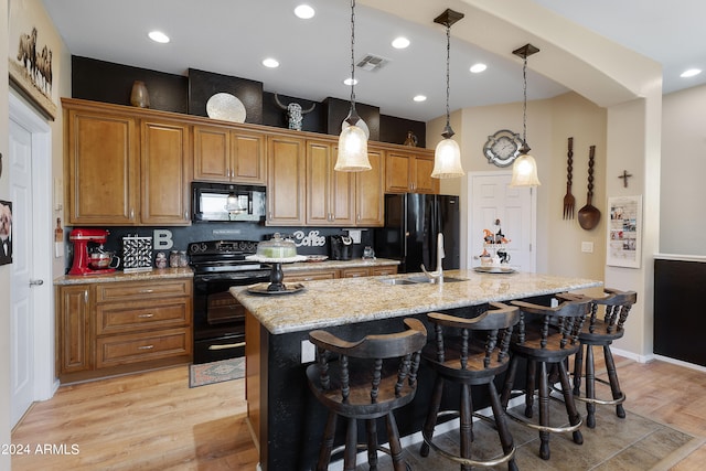 kitchen with an island with sink, hanging light fixtures, black appliances, a breakfast bar, and light wood-type flooring