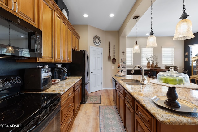 kitchen with light hardwood / wood-style flooring, decorative light fixtures, sink, light stone counters, and black appliances