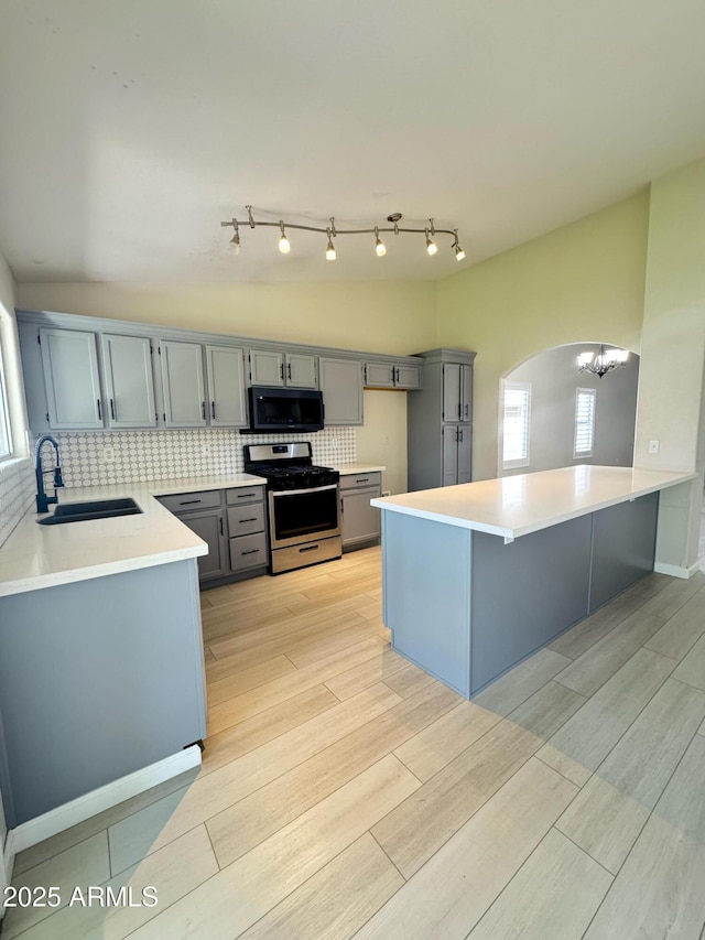 kitchen with a sink, black microwave, stainless steel gas stove, wood finish floors, and gray cabinets