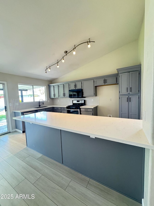 kitchen featuring tasteful backsplash, vaulted ceiling, a peninsula, gray cabinetry, and gas range