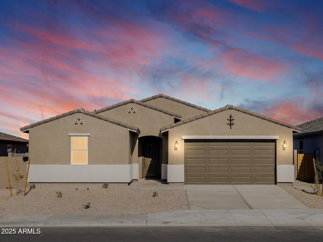 view of front facade with fence, stucco siding, an attached garage, driveway, and a tile roof