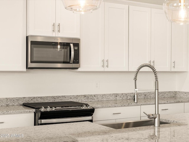 kitchen with stainless steel appliances, light stone countertops, white cabinetry, and a sink