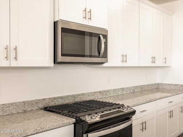 kitchen with stainless steel appliances, light stone countertops, and white cabinetry