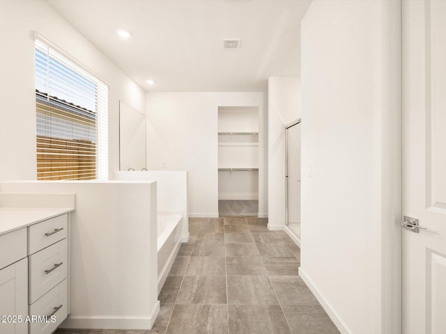bathroom with vanity, recessed lighting, baseboards, a spacious closet, and a bath
