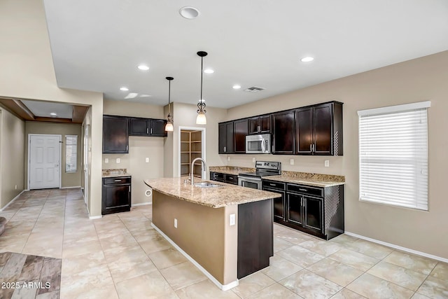 kitchen with a center island with sink, sink, appliances with stainless steel finishes, decorative light fixtures, and light stone counters