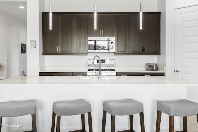 kitchen featuring a sink, appliances with stainless steel finishes, a breakfast bar area, and dark brown cabinets