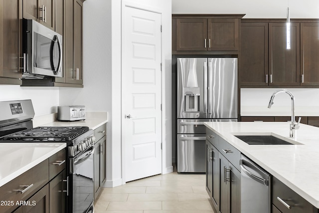 kitchen with light stone countertops, a sink, dark brown cabinetry, appliances with stainless steel finishes, and decorative light fixtures