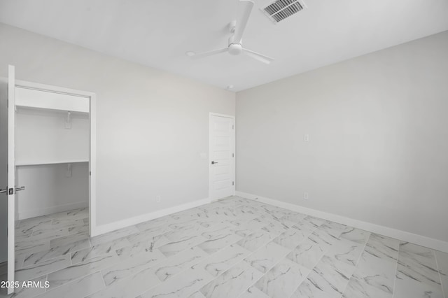 unfurnished bedroom featuring ceiling fan, visible vents, baseboards, marble finish floor, and a walk in closet