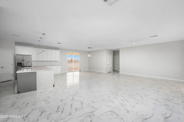 kitchen with marble finish floor, light countertops, open floor plan, white cabinets, and an island with sink