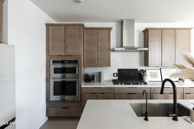 kitchen featuring stainless steel appliances, light stone counters, decorative backsplash, wall chimney exhaust hood, and sink