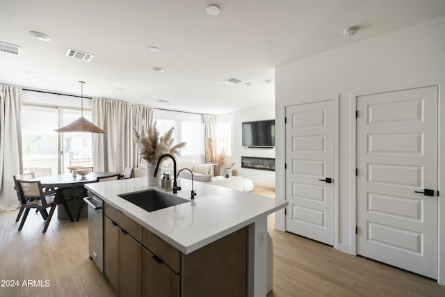 kitchen with sink, light hardwood / wood-style floors, a kitchen island with sink, and pendant lighting