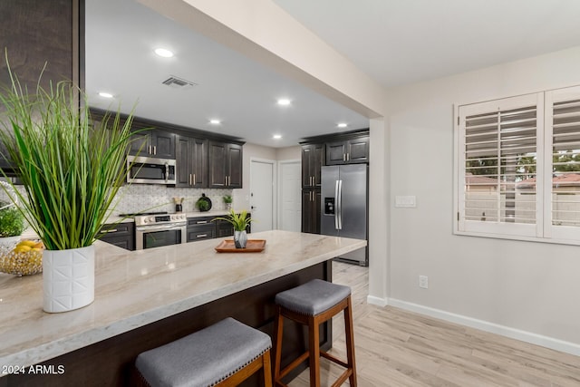 kitchen with tasteful backsplash, light hardwood / wood-style flooring, kitchen peninsula, a kitchen bar, and appliances with stainless steel finishes