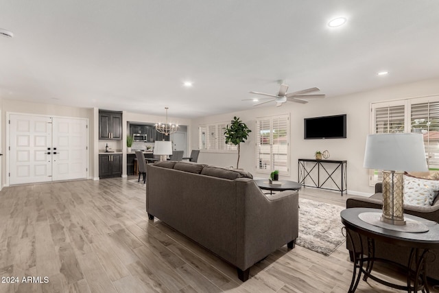 living room featuring ceiling fan with notable chandelier and light hardwood / wood-style floors