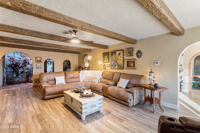 living room featuring ceiling fan, beam ceiling, light wood-type flooring, and a textured ceiling