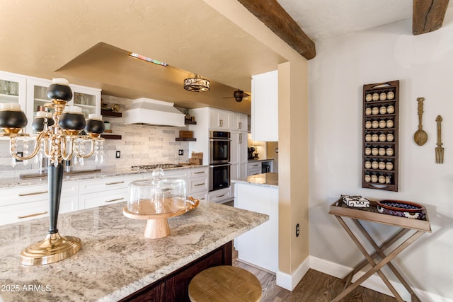 kitchen with premium range hood, white cabinets, light stone countertops, appliances with stainless steel finishes, and a breakfast bar area