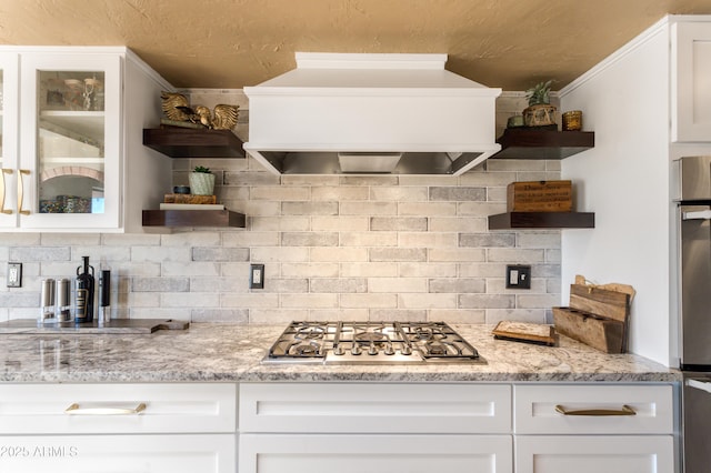 kitchen featuring backsplash, custom range hood, light stone counters, white cabinetry, and stainless steel gas cooktop