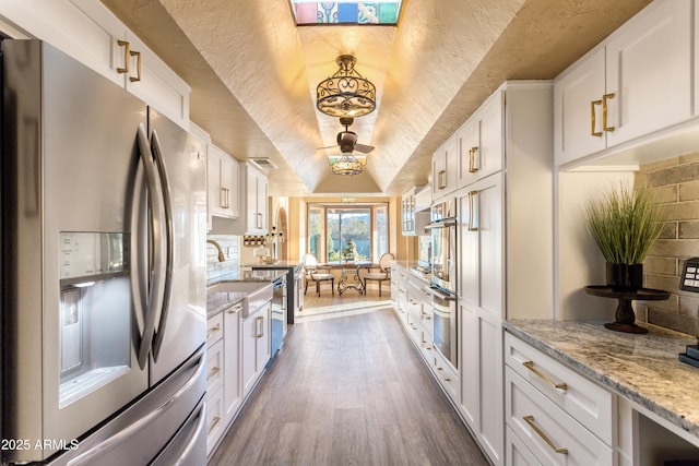 kitchen featuring light stone countertops, stainless steel appliances, pendant lighting, dark hardwood / wood-style floors, and white cabinetry