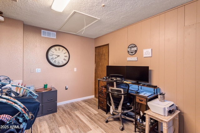 office space with wood walls, a textured ceiling, and light wood-type flooring