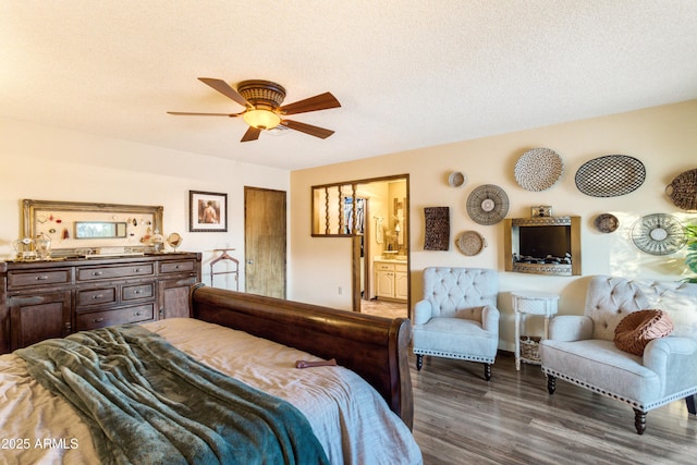 bedroom with a textured ceiling, ceiling fan, dark wood-type flooring, and connected bathroom