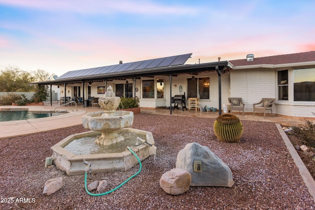 back house at dusk featuring solar panels and a patio