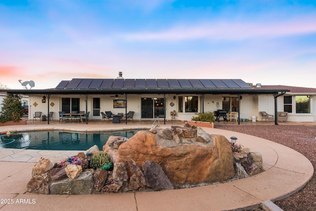 back house at dusk featuring solar panels, a patio, and ceiling fan